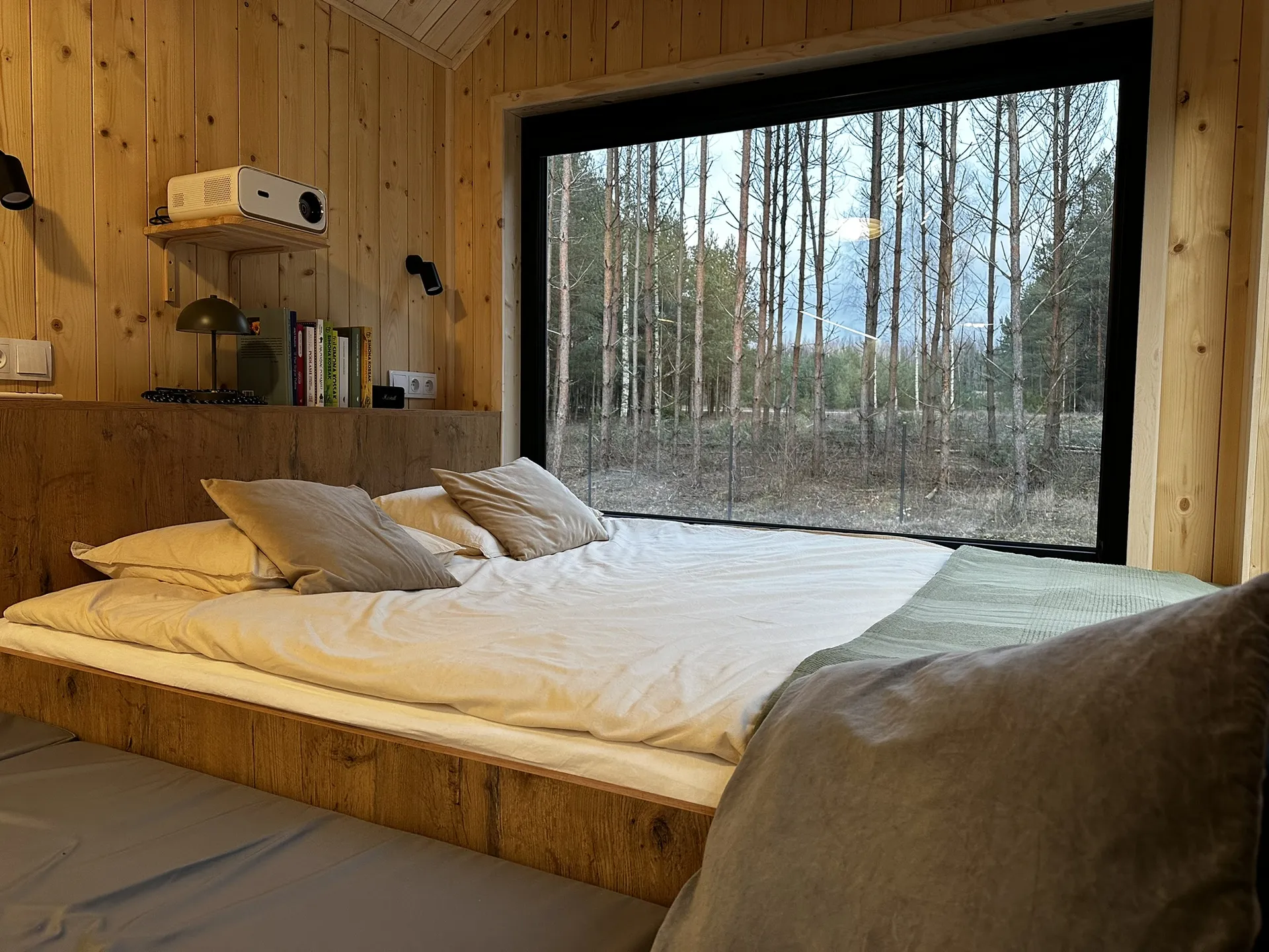Przytulna sypialnia w drewnianym domku mobilnym z dużym oknem na las.